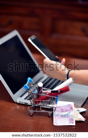 Woman's items and cosmetics in shopping cart, Woman's hands using mobile phone, money, laptop and credit card, Beauty online shopping concept