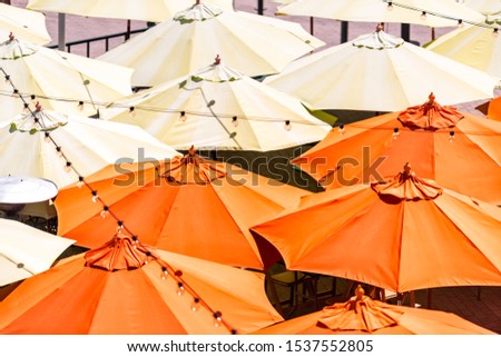 Many colorful yellow orange umbrellas high angle aerial bird's eye closeup view at cafe or restaurant in city during day with hanging light bulbs