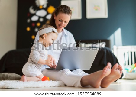 Young mother developing skills of her child with digital tools, watching educating cartoons and programs for kids online. Female freelancer working from home while sitting and taking care of children.