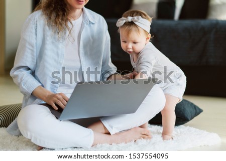 Little girl standing near laptop held by mother and pointing at screen. Mother showing educating videos for developing children's skills. Watch favorite cartoons and shows online sitting in comfort.