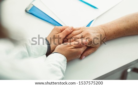 Young doctor's hands are holding the hands of an elderly patient woman as a sign of support.