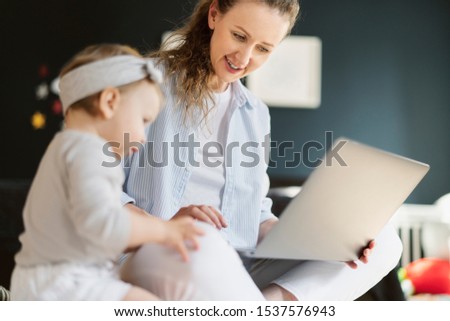 Smiling mom showing daughter funny pictures and photos on laptop. Early development programs for toddlers online. Baby girl watching cartoons on computer with mother. Digital tools, channels and tv.