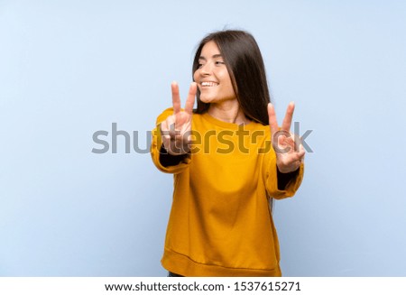 Caucasian young woman over isolated blue wall smiling and showing victory sign