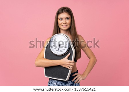 Young girl with weighing machine over isolated pink background