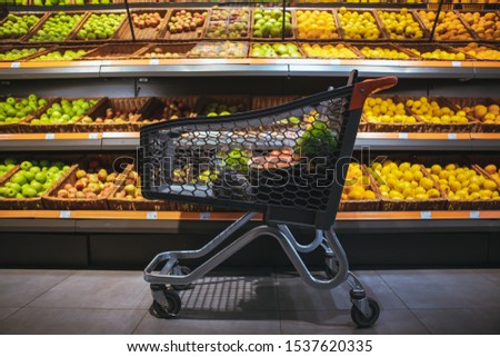 shopping cart in the middle of the picture shelf with oranges and apples on background