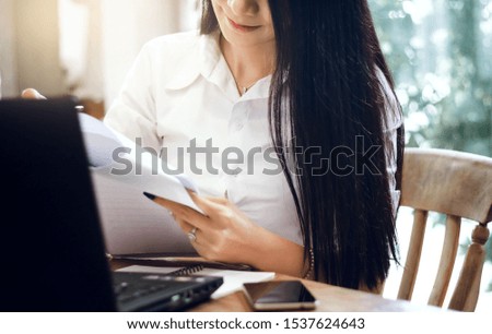 Closeup of asian businesswoman working with laptop and looking on paperwork in hand