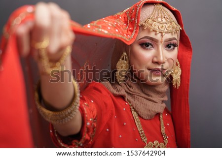 Beautiful hijab girl wearing red traditional India costume lehenga choli or saree with kundan jewelry set isolated over grey background. Deepavali celebration and Bollywood concept