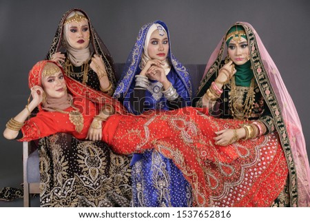 Beautiful hijab girls wearing traditional India costume lehenga choli or saree with kundan jewelry set posing on a couch  over grey background. Deepavali celebration and Bollywood concept