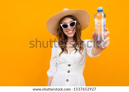 stylish brown-haired woman with a smile on a yellow background, holding a water bottle in her hands, photo with depth of field