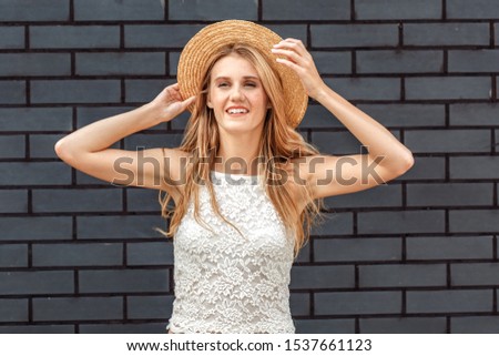 Young girl holding hat windy weather standing isolated on brick wall looking aside smiling happy