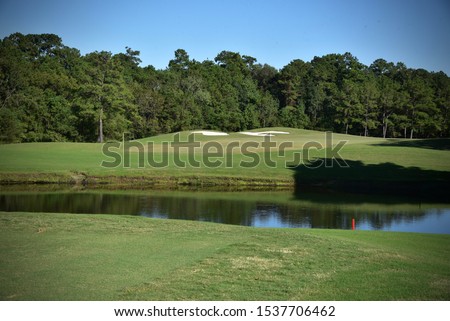 Golf course landscape picturing a water hazard, sand traps and green on a beautiful sunny day.