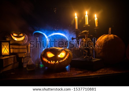 Wizard's Desk. Horror Halloween concept. Magic potions in bottles on wooden table with books and candles. Halloween still-life background with different elements on dark toned foggy background. 