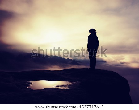 Silhouette of a cow girl or cowboy stay on rocky  edge and watching  down in the mist behind her or him