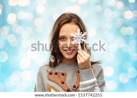 christmas, people and holidays concept - happy young woman with snowflake decoration wearing ugly sweater over festive lights on blue background