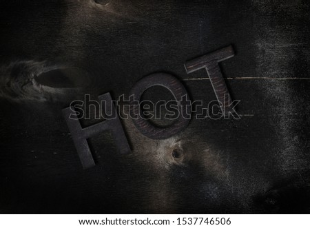 Inscription hot of charred letters  on black wood background