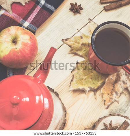 Hot tea, warm blanket, apple, cinnamon sticks, anise star and autumn leaves on old wooden background, vintage toned photo. Top view, flat lay.