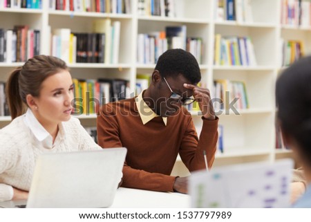 Portrait of African-American student thinking while studying in college class, bookshelves in background, copy space
