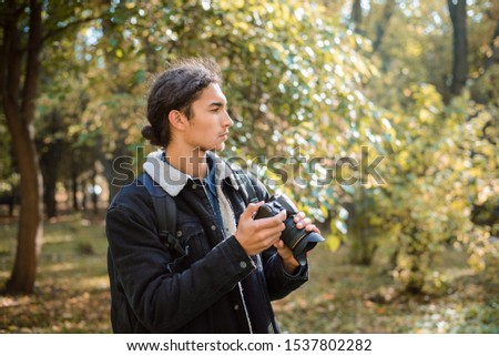 Portrait of photographer with modern photography equipment looking for good composition or interesting thing to shoot, standing in autumn forest
