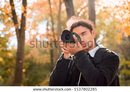 handsome man photographer takes pictures in the Autumn forest, looking through the viewfinder of his modern high-end camera, looking for perfect composition