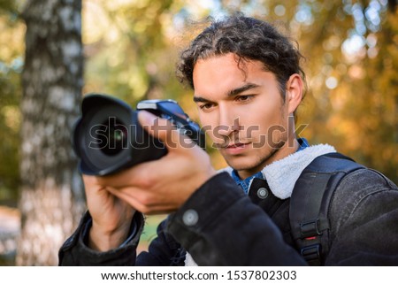 Young male photographer photographing nature. Consentrated student photographer shooting autumn landscape in forest in the morning