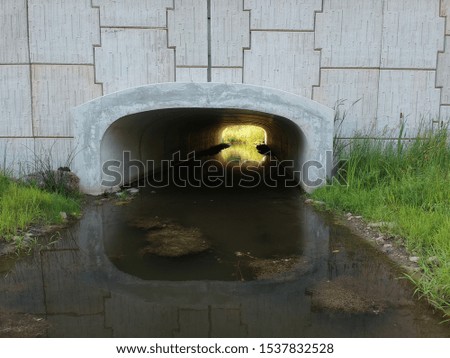 Water flowing under through a tunnel under a concrete bridge. Pattern on the side wall of the bridge.