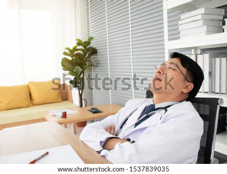 Young handsome Asian Doctor with short black hairs so tired of hard work all day long then fall asleep at work in the Hospital. background - copy space. 