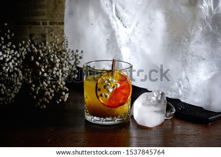 orange Cocktail with iceball and dry white flowers on the wooden table with dark light