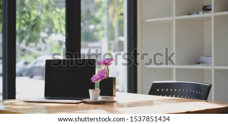 Open blank screen laptop computer in comfortable workspace with pink flower in tree pot 