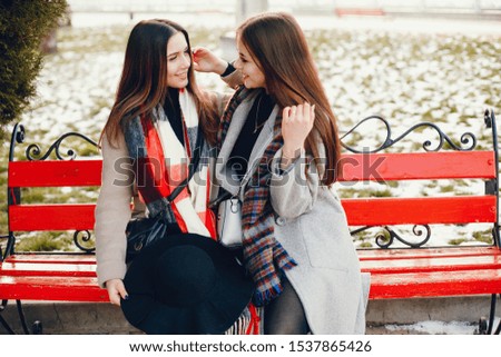 Fashionable girls in a winter city. Stylish ladies in a coats. Women sitting on a bench