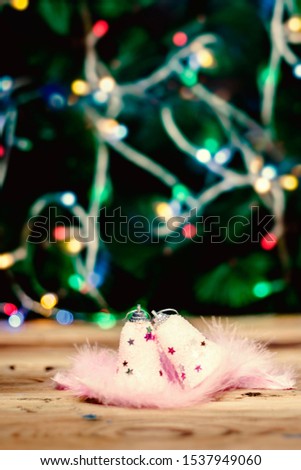 Cute pink Christmas toys with light pink feathers on wooden table against Christmas tree on background