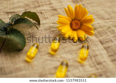 Close up yellow calendula flower at linen fabric with blurred fish oil capsules and raspberry leaf, soft focus, alternative medicine concept, soft focus