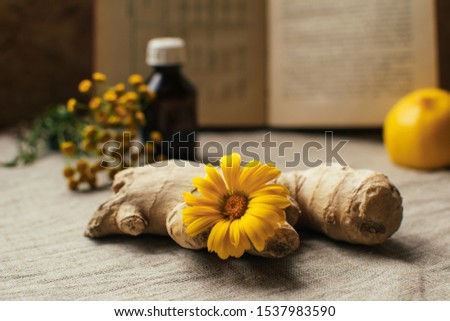 Traditional medicine background with ginger and calendula at blurred vintage recipy book, lemon, pharmacy bottle, tansy at the table covered by linen textile, copy space