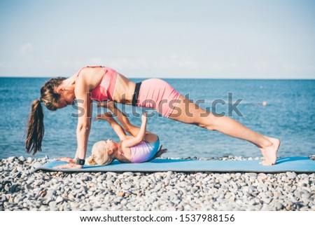 Family workout - mother and daughter doing exercises on beach at the morning. Healthy lifestyle.