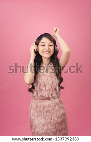 Happy joyful asian woman in headphones listening to music and dancing isolated over pink background