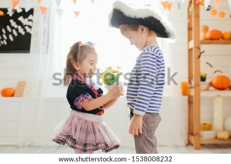 Boy in a pirate costume and a girl in a witch costume celebrates Halloween at home. A boy gives flowers to a girl.