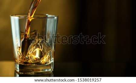 Pouring whiskey into glass in freeze motion. Free space for text, dark background.