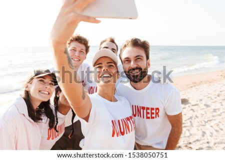 Group of happy young friends volunteers making a selfie while standing at the beach together