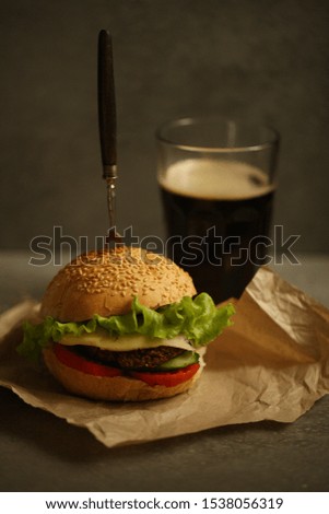 The Burger with the greens and chop on Kraft paper with a drink