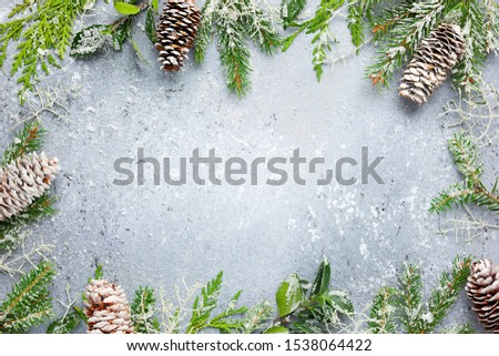 Christmas or winter background with a border of green and frosted evergreen branches and pine cones on a grey vintage board. Flat lay, winter concept with copy space.