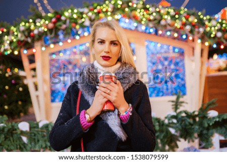 Picture of blonde woman with glass in hands against background of burning garlands in street