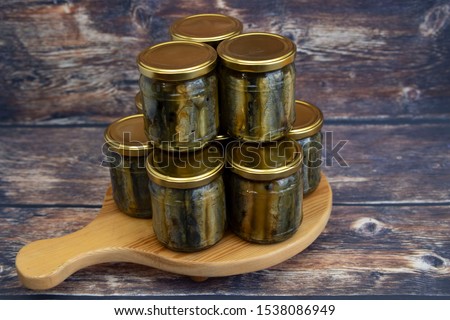 Homemade canned fish. Fried lamprey, cut into pieces in glass jars with marinade, spices and gelatin. Pyramid on a wooden board. Royalty-Free Stock Photo #1538086949