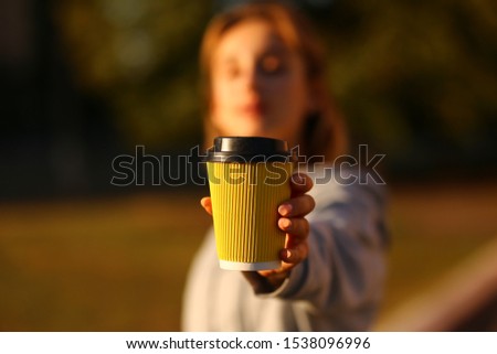 Girl showing paper cup of coffee in his hands close up. American paper eco cup. Girl drinking coffee indoors.