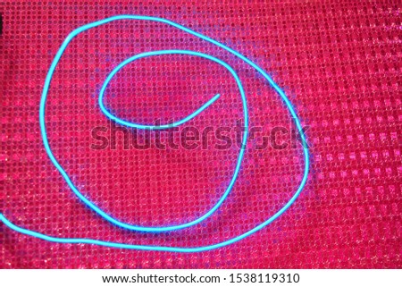 Blue glowing wire, cold neon, electroluminescent cord, cable lies on a holographic pink background with various types of overflow.