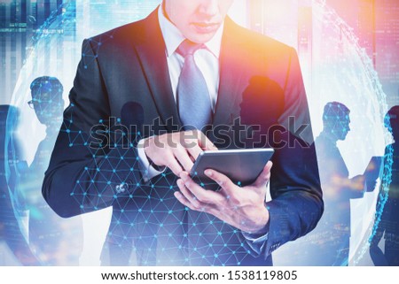 Young businessman with tablet using it in modern city with his colleagues in background and double exposure of planet hologram. Concept of internet connection. Toned blurry image