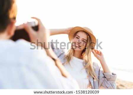 Beautiful happy young couple spending time at the beach, man taking pictures of his girlfriend