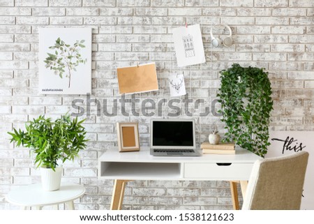 Comfortable workplace with mood board and laptop near brick wall