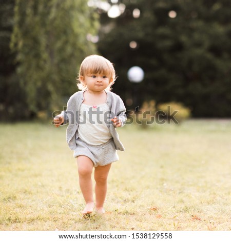 Pretty baby girl 1-2 year old walking in park over nature background. Summer season. Childhood. 