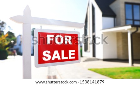 Red real estate sign near house outdoors on sunny day