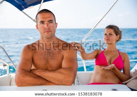 Young woman talking to offended husband during sea travel on yacht

