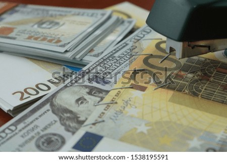 The stapler fastens the dollar and euro notes with iron clips. Stapler with paper clips on the background of banknotes. Counterfeit money